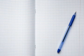A blue ball pen lying on a blank checkered school notebook sheet , paper with copy space