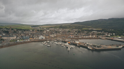 Fototapeta na wymiar Ships, yachts at sea bay aerial. Cityscape with ancient architecture landmark at ocean pier town Campbeltown, Scotland, Europe. Dramatic streets: old buildings at highway with driving cars at dusk day