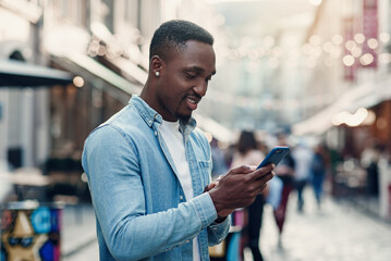 Young african american man standing on the summer street and using smart phone.