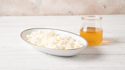 White cottage cheese with a maple syrup in a jar beside on a wooden table. Healthy breakfast of fresh cottage cheese