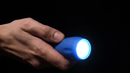 Hand with a led flashlight shining in the darkness with blue beam into the camera, spy and investigation concept - obrazy, fototapety, plakaty