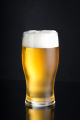 A cold glass of craft light beer on a black background with dew and foam With a place for your text.