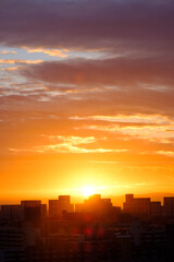 都市の夜明け、早朝ビルの隙間から太陽が昇り辺りはオレンジ色に染まる。ビルはシルエットに浮かぶ