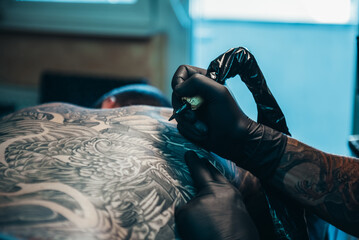 Tattoo artist hands wearing black gloves and holding a tattoo machine