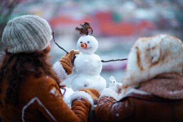 mother and child outside in city park in winter making snowman