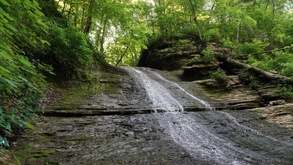 Water runoff flowing down incline rock face in woods forest