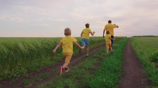 Family run of father and sons in park. Happy family team, scampering together in the field, joyfully waving their hands. Sons, children, dad run, play, rejoice, enjoy nature in summer. Family teamwork