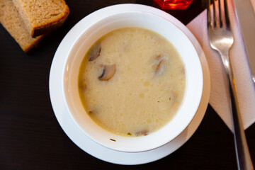 Portion of fresh mushroom soup served in soup bowl with serving pieces and brea