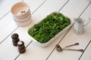 recipiente con verduras Kale sobre una mesa blanca junto a recipientes y condimentos