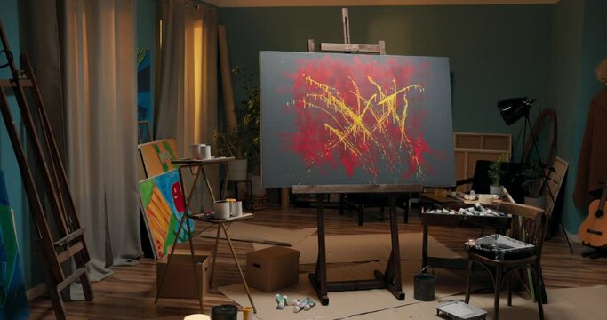 Abstract modern painting in yellow and red colors standing on an easel in a home office, studio, talented artist working in art disorder, around painting accessories
