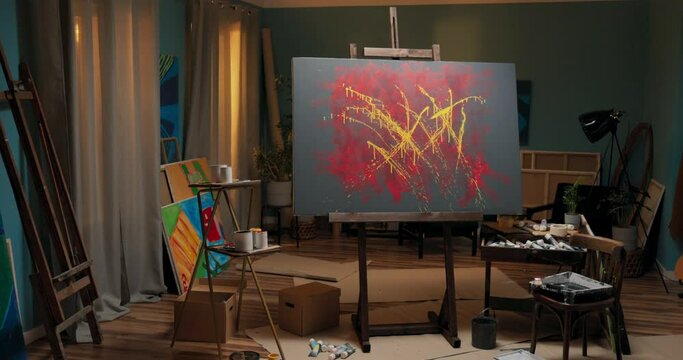 Abstract modern painting in yellow and red colors standing on an easel in a home office, studio, talented artist working in art disorder, around painting accessories