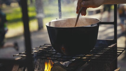 stirring food in a pot with your hand, cooking food on fire in a camping trip in nature, recipes...