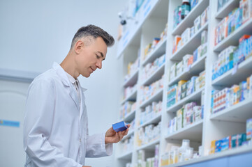 Pleased man in lab coat reviewing medications at pharmacy