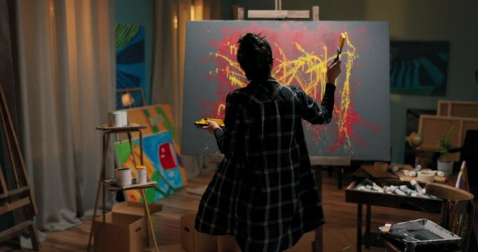 Talented painter spends evening in front of canvas devotes time to abstract work, in hand holds can of yellow paint and brush, girl splashes color on painting, artistic vision