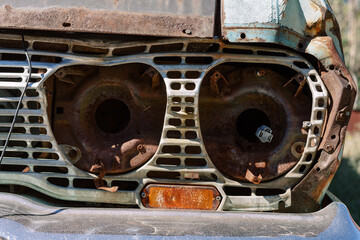 The head light of an old vintage retro car rusts and oxidizes outside in a salvage junk yard