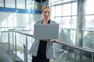 Woman with suitcase and open laptop standing at airport