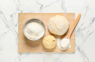 Board with fresh dough and flour on light background