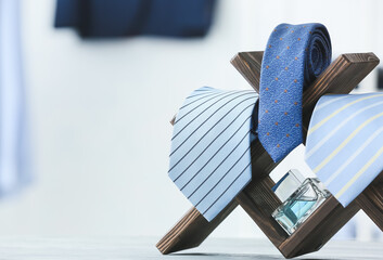 Stand with stylish neckties and perfume on table, closeup