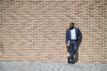 Fototapeta na wymiar An african american man in a suit standing near the brick wall