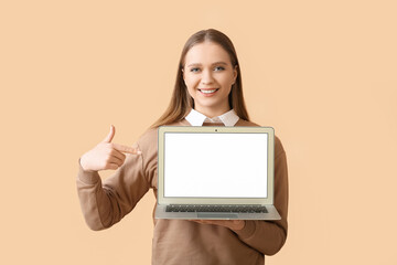 Beautiful young woman holding laptop with blank screen on color background