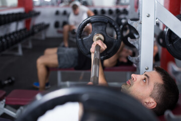 Sporty man performing weightlifting workout at gym, exercising with barbell.