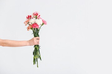 Hand with bouquet of beautiful carnations on light background