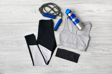 Sportswear, skipping rope and bottle for water on light wooden background