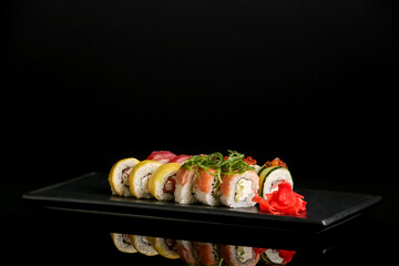Tray with tasty sushi rolls, chuka and ginger on dark background