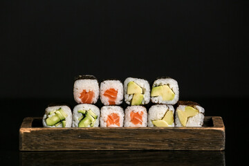 Wooden tray with delicious salmon and avocado maki rolls on dark background © Pixel-Shot