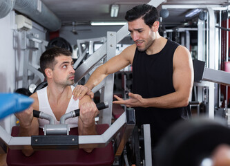 Fototapeta na wymiar Portrait of sporty man during strength training with personal instructor in gym