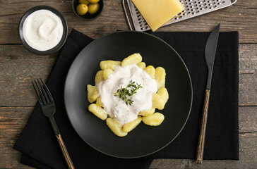 Plate of delicious gnocchi with creamy sauce on wooden background