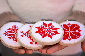 Woman holding hand made cross stitch folk Christmas decoration ornament embroidery on plywood. Nordic snowflakes. - obrazy, fototapety, plakaty