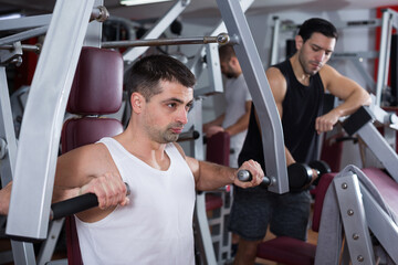 Sporty guy training muscles of arms and shoulder girdle on fitness machine in gym