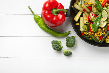 Frying pan with different vegetables on light wooden background