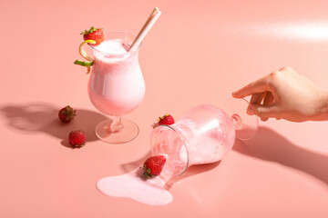 Female hand with glass of strawberry Pina Colada cocktail spilled on color background