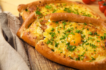 Board with tasty Ajarian khachapuri on wooden background, closeup