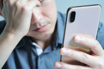 young man sitting down His face was unsettled. And he looked at his smartphone with a headache and strain. Causes of hard work and insufficient rest