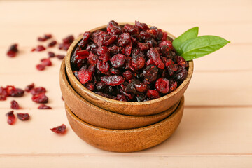 Bowl with tasty dried cranberries on color wooden background, closeup