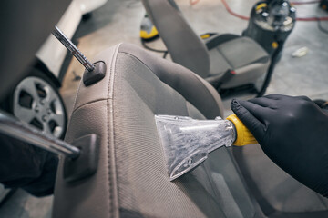 Fototapeta na wymiar Vacuum cleaning and drying of leather seat by car service technician