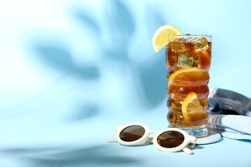 Glass of refreshing Long Island iced tea, sunglasses and towel on color background