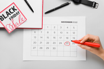 Woman marking date of Black Friday in calendar on grey background