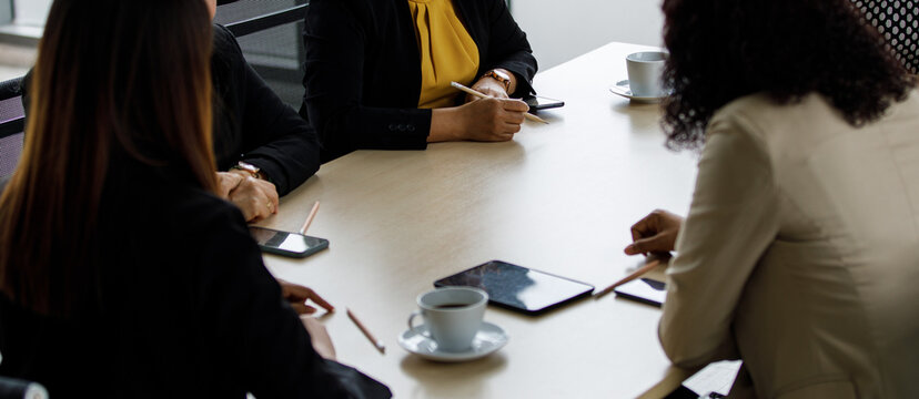 Group of businesswomen in formal business clothing sitting together around meeting table taking note in conference room brainstorming discussing planning about working marketing strategy in company