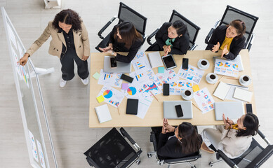 High view of six business women working and one woman presenting charts and graphs papers with tablets and laptops on the table. Concept for business meeting