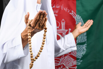 Praying Muslim man with tasbih against flag of Afghanistan