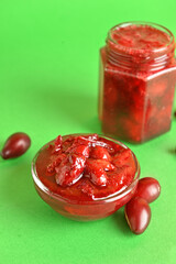 Bowl and jar with tasty dogwood jam on green background