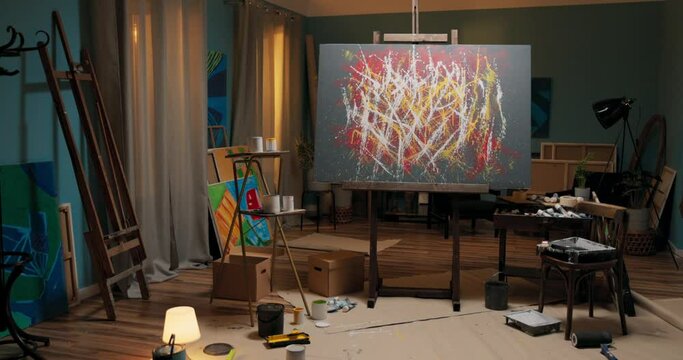 Abstract modern crazy painting in yellow red white colors standing on easel in home office, studio, talented artist working in art disorder, around painting accessories