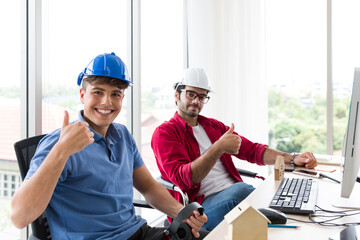 Two engineering man wear helmet working at office desk at work with happy and smile. Group of technical men wear casual working together in the office with desktop computer
