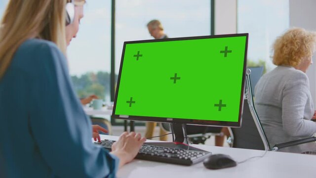 Over shoulder view of computer monitor. Woman typing on keyboard. Modern open space office interior.