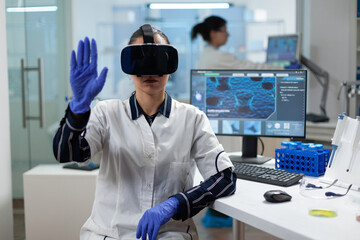 Biologist researcher wearing virtual reality headset examining biochemistry experiment working in microbiology hospital laboratory using biotechnology. Specialist scientist analyzing virus development