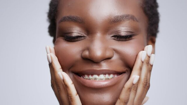 Young beautiful happy african american woman with dental braces caressing her face, enjoying freshness and beauty